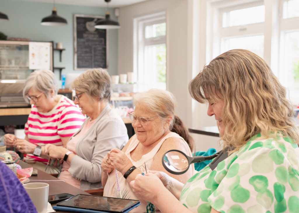 small group of mature adults sitting around a table knitting at north end bakery