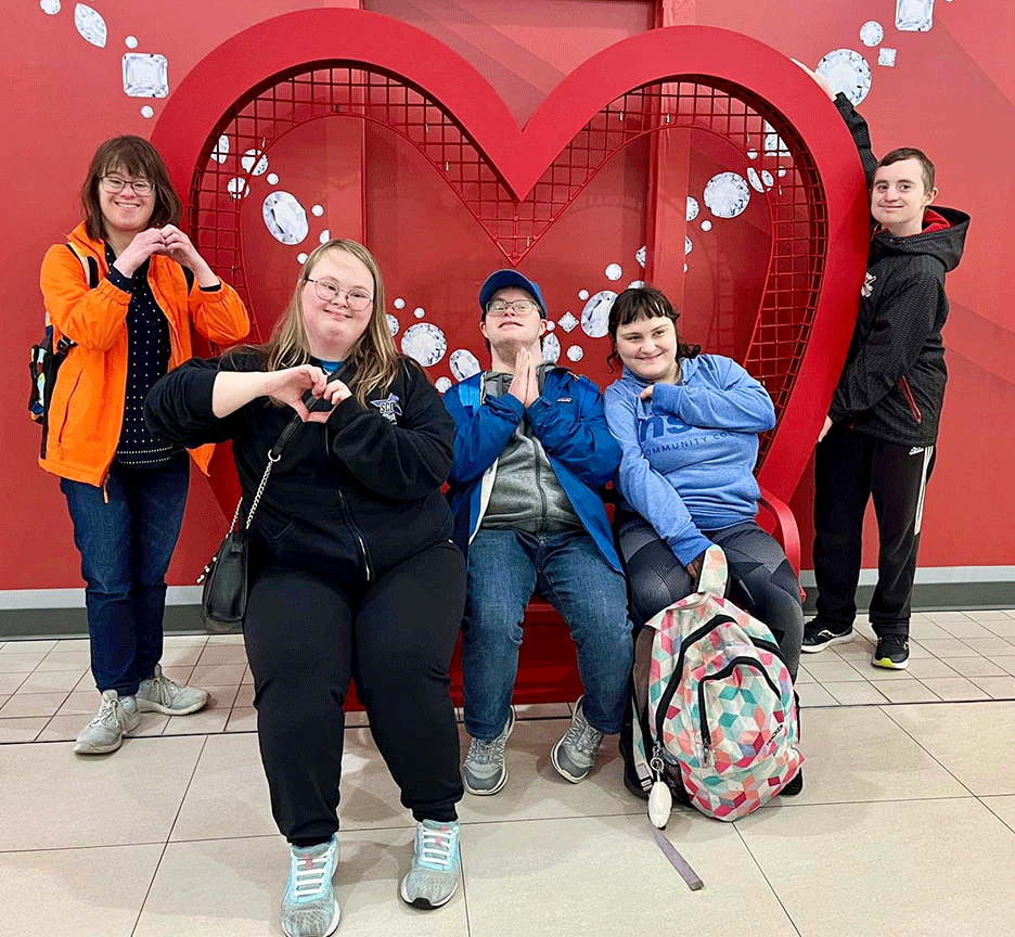 smiling participants pose together in front of a large red heart