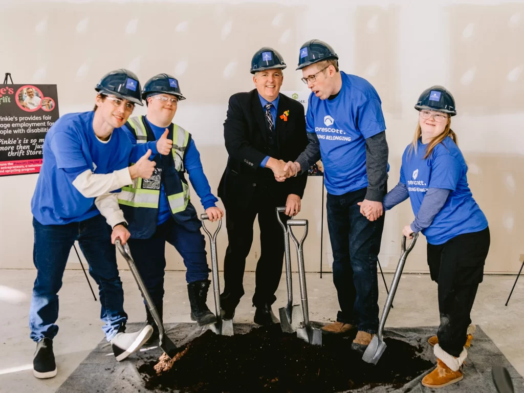 A ceremonial ground-breaking ceremony, where community members in matching blue t-shirts use shovels in a small patch of dirt.