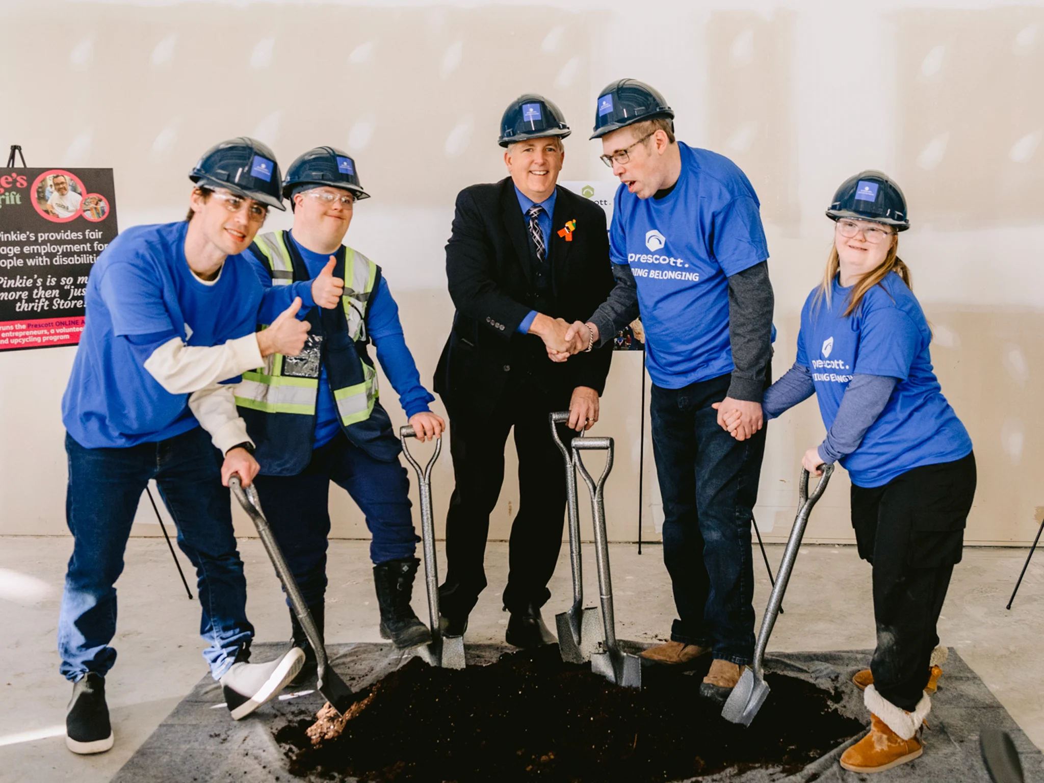 A ceremonial ground-breaking ceremony, where community members in matching blue t-shirts use shovels in a small patch of dirt.
