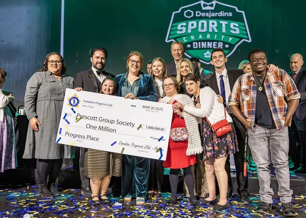 members of prescott group are on stage at a fundraising event posing for a picture with a ceremonial cheque.